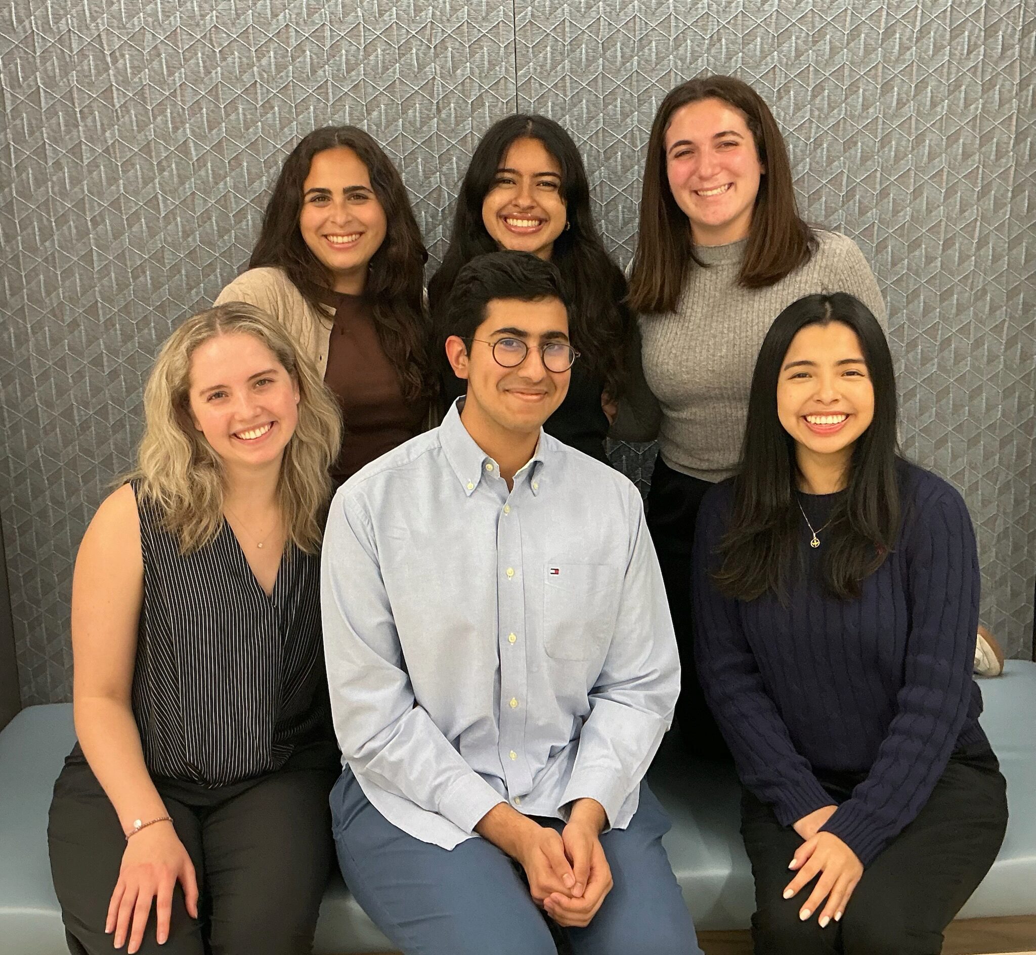 A small group of smiling individuals posed together in front of a textured wall.