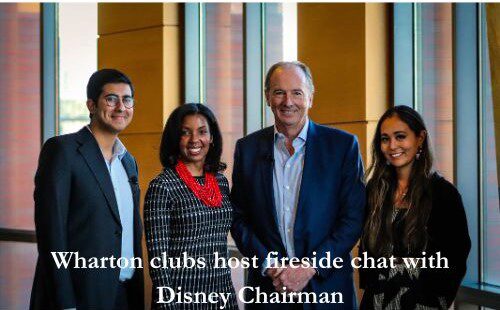 A small group of people stands together smiling, dressed in business attire. Text reads, "Wharton clubs host fireside chat with Disney Chairman."